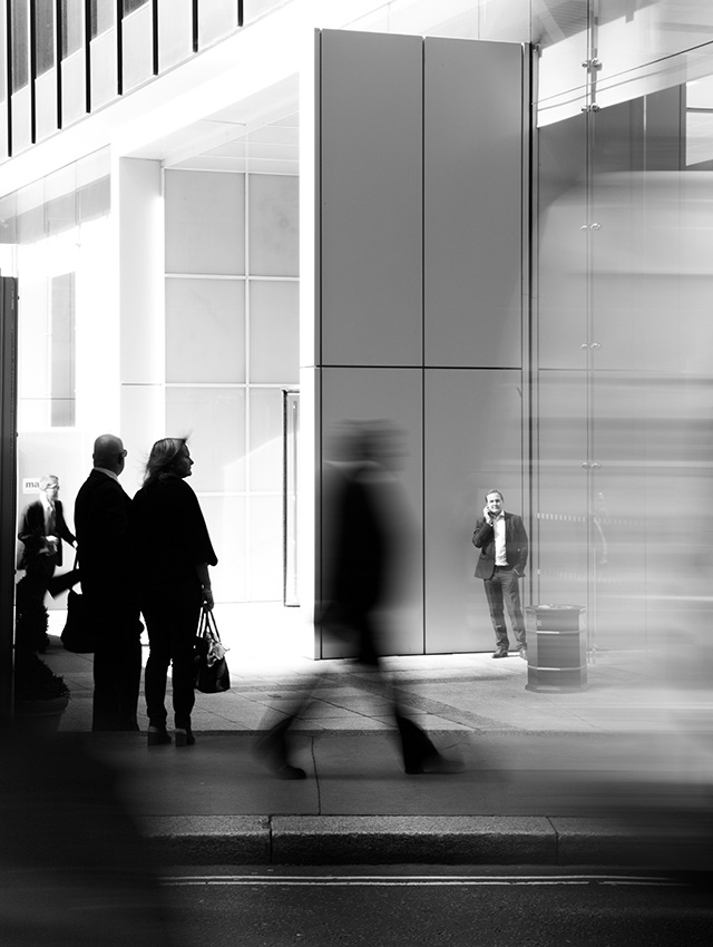 Menschen gehen auf dem Bürgersteig vor einem Hochhaus vorbei